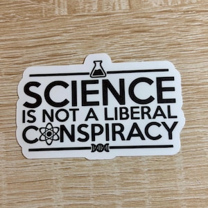 May include: White sticker with black text that reads "SCIENCE IS NOT A LIBERAL CONSPIRACY." The sticker includes a beaker and an atom symbol. The sticker is rectangular with a white border.