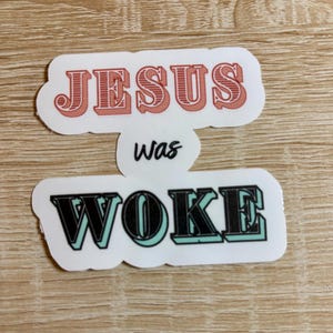 May include: Two stickers with the text "JESUS was WOKE" in a retro font. The top sticker is red and the bottom sticker is white with black and teal lettering.