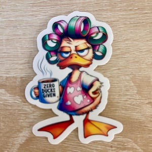May include: A cartoon duck with pink and green curlers in her hair, wearing a pink shirt with white hearts, holding a coffee mug that says "Zero Ducks Given".