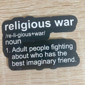 Pu&ograve; includere: Un adesivo nero con la scritta "religious war" in bianco e una definizione. La definizione recita: "1. Adulti che litigano su chi ha il miglior amico immaginario."