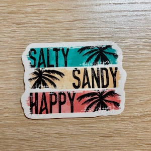 May include: A sticker with a distressed, vintage look featuring three horizontal stripes in turquoise, yellow, and pink. Each stripe has a palm tree silhouette and text. The text reads "Salty", "Sandy", and "Happy".