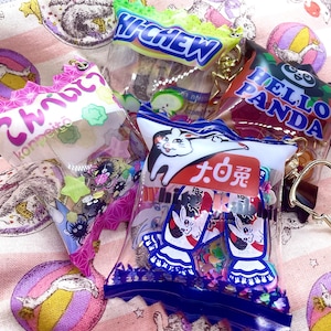 Puede incluir: Cuatro bolsas de plástico transparentes con diseños y textos coloridos. Las bolsas contienen varios artículos pequeños, como caramelos, pegatinas y abalorios. Las bolsas cuelgan de cadenas doradas.