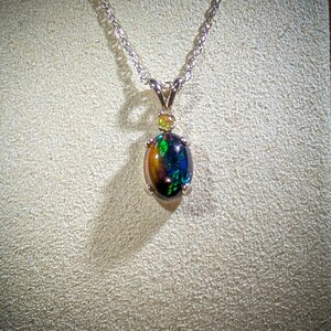 May include: A silver chain necklace with a black opal pendant. The opal is surrounded by small, clear gemstones.