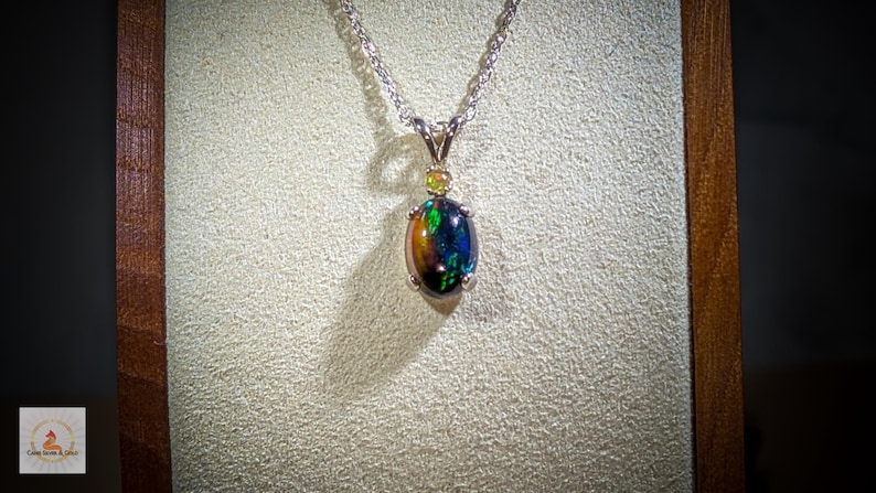 May include: A silver chain necklace with a black opal pendant. The opal is surrounded by small, clear gemstones.