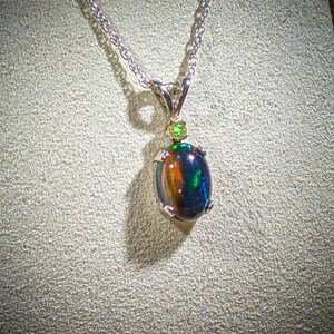 May include: A silver chain necklace with a black opal pendant accented with two green gemstones.