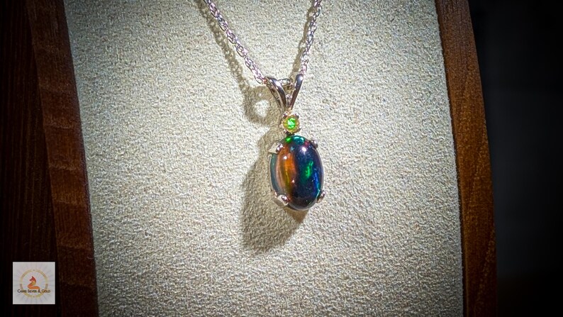 May include: A silver chain necklace with a black opal pendant accented with two green gemstones.