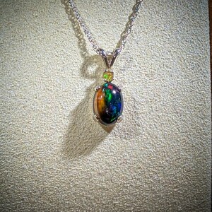 May include: A silver chain necklace with a pendant featuring a black opal gemstone surrounded by smaller green gemstones.