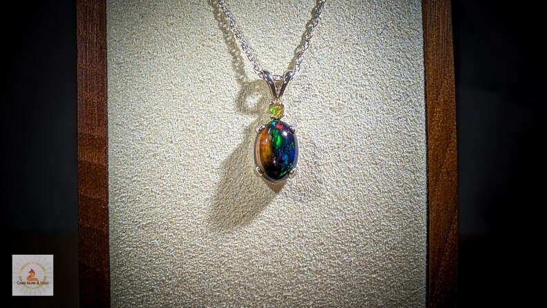 May include: A silver chain necklace with a pendant featuring a black opal gemstone surrounded by smaller green gemstones.