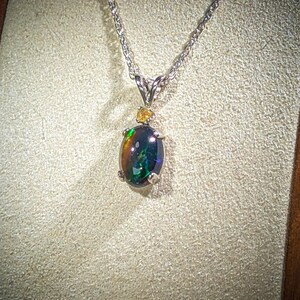 May include: A silver chain necklace with a black opal pendant. The opal is surrounded by small, clear stones.