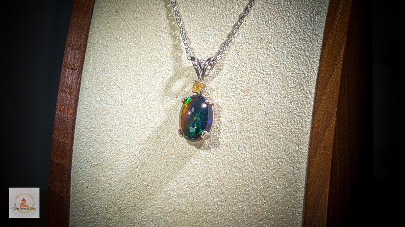 May include: A silver chain necklace with a black opal pendant. The opal is surrounded by small, clear stones.