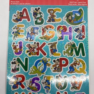 May include: A sheet of die-cut stickers featuring the alphabet with Disney characters. The stickers have a glittery finish and are in various colors. The top of the sheet has the text "Die-Cut Stickers" and "Photo-Safe".