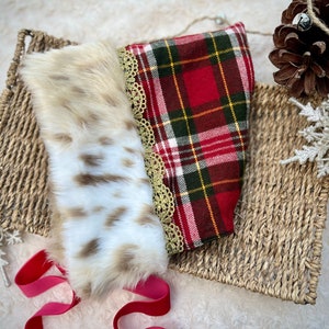 May include: A red and green plaid fabric with a white lace trim and a white faux fur trim. The fabric is lying on a woven basket.