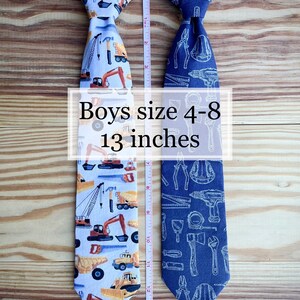 May include: Two boys' ties, one with a construction vehicle pattern and the other with a tools pattern. Both ties are 13 inches long and are suitable for boys sizes 4-8.
