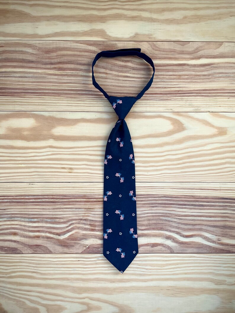 May include: A dark blue tie with a pattern of small American flags. The tie is made of a smooth fabric and has a classic design.