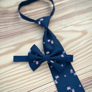 May include: A navy blue bow tie and matching necktie with a pattern of small American flags. The bow tie has a white star pattern.