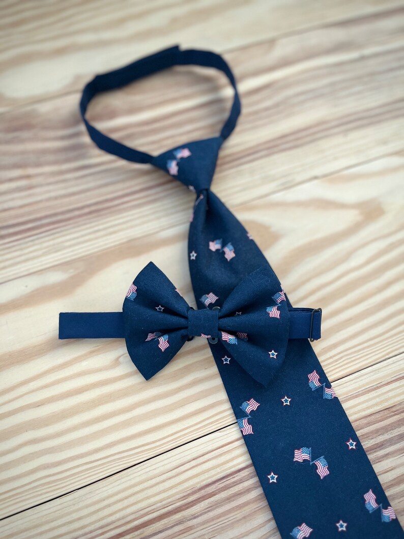 May include: A navy blue bow tie and matching necktie with a pattern of small American flags. The bow tie has a white star pattern.
