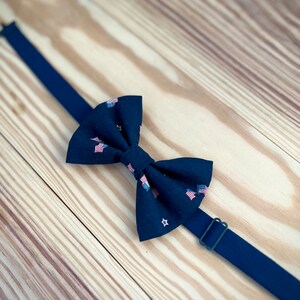 May include: A black bow tie with a pattern of small American flags and stars. The bow tie is on a wooden surface.