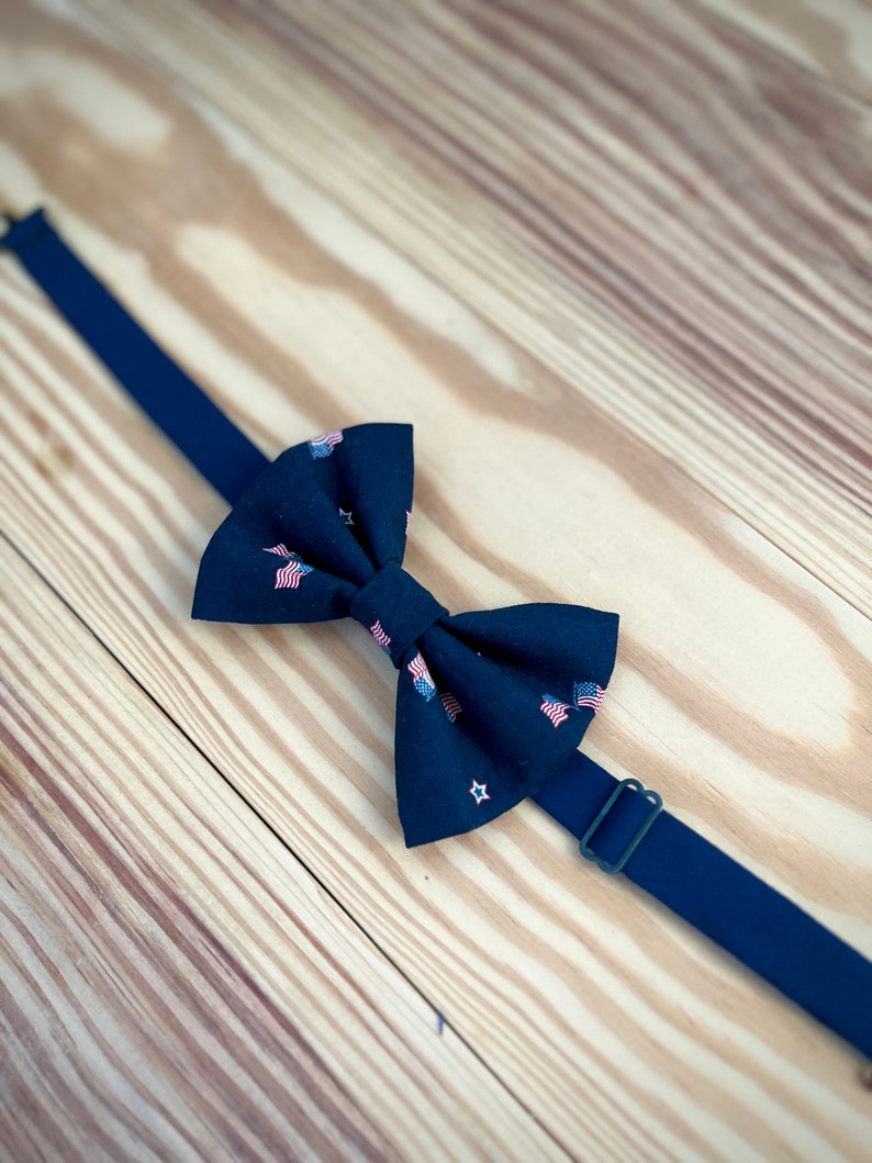 May include: A black bow tie with a pattern of small American flags and stars. The bow tie is on a wooden surface.