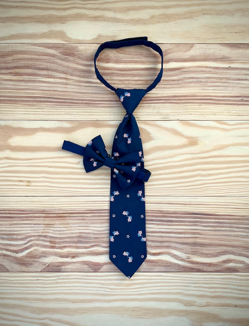 May include: A dark blue tie with a pattern of small American flags and white stars. A matching bow tie is also included.