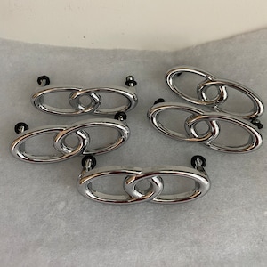 May include: Five silver-toned cabinet knobs with a linked oval design. The knobs have a polished finish and are suitable for kitchen or bathroom cabinets.