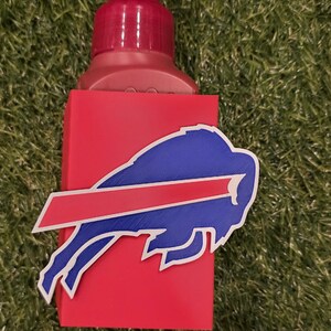 May include: A red soap dispenser with a red pump and a blue and red Buffalo Bills logo. The dispenser is on a green surface.