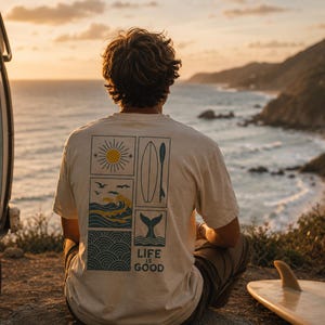 Pu&ograve; includere: Una t-shirt beige a maniche corte con una stampa grafica sul retro. Il design include quattro pannelli rettangolari che mostrano un sole giallo, una tavola da surf, una pagaia, onde oceaniche con uccelli e una coda di balena, con il testo "LIFE IS GOOD".