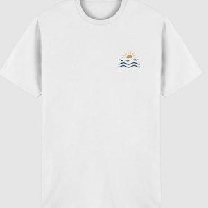 Pu&ograve; includere: Una t-shirt bianca a maniche corte con una piccola grafica sulla parte superiore sinistra del petto. La grafica raffigura un sole giallo che sorge sopra due linee ondulate blu scuro che rappresentano l'acqua, con tre piccoli uccelli blu scuro.