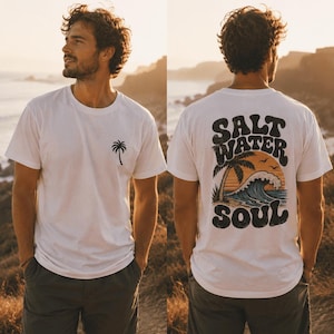 May include: White t-shirt with a palm tree graphic on the front and "Salt Water Soul" design on the back. The back design features a palm tree, waves, and a sunset. The person is wearing dark green shorts.