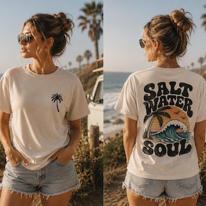 Könnte beinhalten: Ein cremefarbenes Kurzarm-T-Shirt mit einer kleinen schwarzen Palme auf der linken Brustseite. Die Rückseite des Shirts zeigt eine große Grafik mit dem Text "SALT WATER SOUL", die eine Palme, eine Meereswelle und eine Sonne umrahmt.
