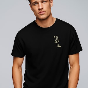 Könnte beinhalten: Schwarzes T-Shirt mit einem minimalistischen Design eines Baumes, einer Sonne und einem Fuchs in Hellbraun. Das kurzärmelige Shirt ist aus einem weichen Material gefertigt. Das Design befindet sich auf der oberen linken Brustseite.