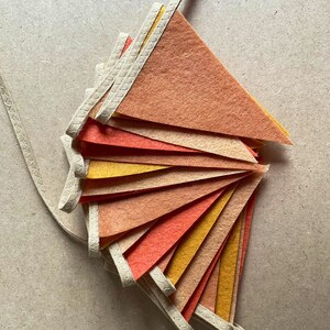 May include: A set of felt pennant flags in shades of orange, yellow, and red. The flags are strung together with a white cord and have a stitched edge.
