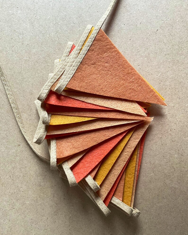 May include: A set of felt pennant flags in shades of orange, yellow, and red. The flags are strung together with a white cord and have a stitched edge.