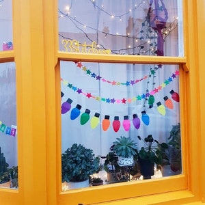 May include: A window with a yellow frame and a colorful string of lights with stars and light bulbs. The window is decorated with a sign that says "33 Stitches".