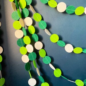 May include: A green and white felt garland with circles strung together. The garland is hanging on a blue wall.