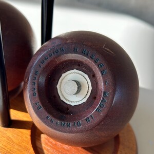 May include: A close-up of a wooden salt shaker with a white grinder. The bottom of the shaker is engraved with "BOOM DESIGN" and "MADE IN DENMARK". The shaker is part of a set on a wooden stand.