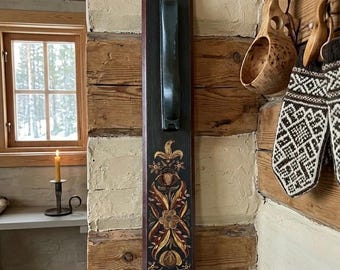 May include: A dark wooden wall-mounted handle with a decorative floral design in gold, red, and yellow. The handle is mounted on a dark brown rectangular board. The background is a rustic wooden wall.