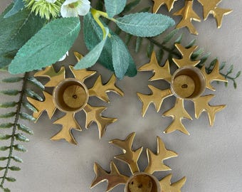 May include: Four gold metal candle holders shaped like snowflakes. Each holder has a round, open top for a candle.