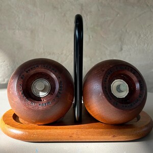 May include: A vintage salt and pepper shaker set. The set includes two round, dark brown wooden shakers with metal mechanisms, resting on a wooden tray. A black metal handle is between the shakers. The words "MADE IN DENMARK" are visible on the shakers.