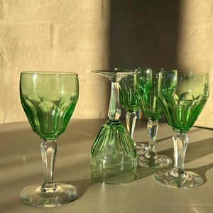 Könnte beinhalten: Eine Sammlung von grün getönten Glasbechern mit klaren Stielen und Böden. Die Becher haben ein dekoratives, geriffeltes Design auf der Schale. Die Gläser sind auf einer hellen Oberfläche angeordnet, wobei ein Becher umgedreht ist.