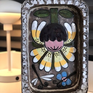 May include: Rectangular ceramic tray with a floral design. The tray has a brown background with a large flower in the centre, accented with yellow, white, and pink petals. A dragonfly and blue flower are also depicted.