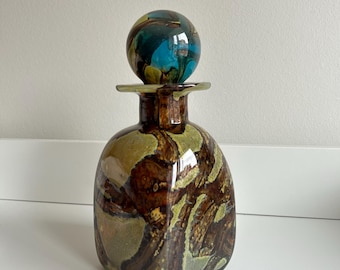 May include: A brown and green glass decanter with a swirl pattern and a blue and green glass stopper.