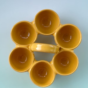 Puede incluir: Una fuente de cer&aacute;mica amarilla con siete compartimentos circulares dispuestos en forma de flor. La fuente tiene un asa y un acabado brillante. Los compartimentos est&aacute;n dise&ntilde;ados para contener peque&ntilde;as porciones de comida.