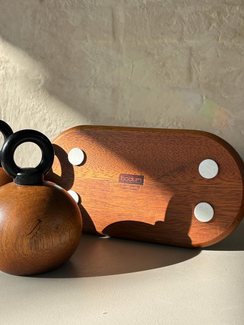 May include: A wooden bottle stopper with a black handle and a round, brown body. A wooden serving tray with white pads is also visible. The tray has the brand name "bodum" printed on it.
