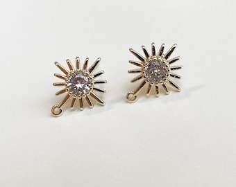 May include: A pair of gold-tone earrings with a starburst design and a clear crystal in the center. The earrings have a small loop at the bottom for attaching to a hook.