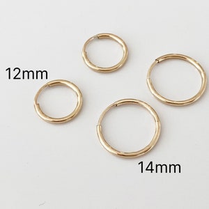 Könnte beinhalten: Vier goldfarbene Creolen in verschiedenen Größen werden vor einem weißen Hintergrund gezeigt. Die Ohrringe haben einen Durchmesser von 12 mm und 14 mm. Das Bild zeigt das schlichte, kreisförmige Design der Ohrringe.
