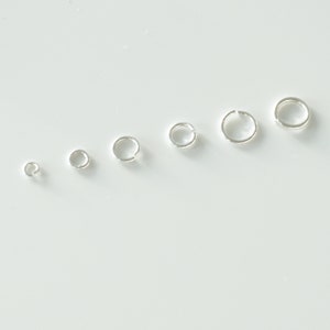 Peut inclure: Sept anneaux de saut en argent de tailles différentes, disposés en ligne du plus petit au plus grand.