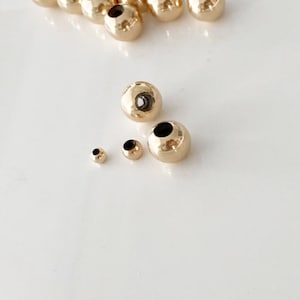 May include: A set of gold-coloured metal beads of varying sizes. The beads are round and have a hollow centre.