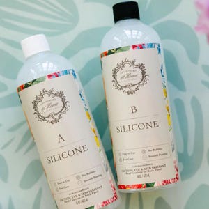 May include: Two clear bottles of silicone with white labels featuring the text "Amy Howard at Home". The labels have floral borders and the letters "A" and "B". Each bottle contains 16 fl oz / 473 ml.