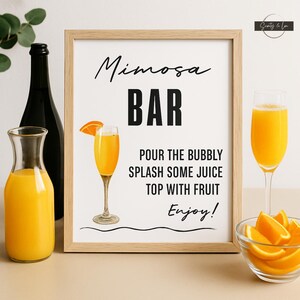 Könnte beinhalten: Eine Mimosa-Bar-Szene mit einem gerahmten Schild, einer schwarzen Flasche, einem Krug mit Orangensaft, zwei Sektgläsern und einer Schüssel mit Orangenspalten. Das Schild lautet "Mimosa BAR" mit Anweisungen.