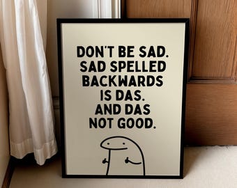 May include: A framed print with the text "DON'T BE SAD. SAD SPELLED BACKWARDS IS DAS. AND DAS NOT GOOD." in black font on a cream background. A simple cartoon figure is at the bottom. The frame is black.